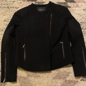 Svart jacka från Xoul Edition - Snygg svart jacka från Xoul Edition med dragkedjor framtill och på fickorna. Den är långärmad och har en normal passform. Stroelek S/M