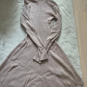 Beige ribbad klänning - Snygg beige ribbad klänning med polokrage och långa ärmar. Perfekt för en stilren look. Tillverkad i en mjuk blandning av viskos och nylon som ger en skön passform.