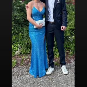 Blå glittrig långklänning - Säljer en blå glittrig balklänning med smala axelband och öppen rygg som är V-ringad där fram. Pris kan diskuteras vid snabb affär!