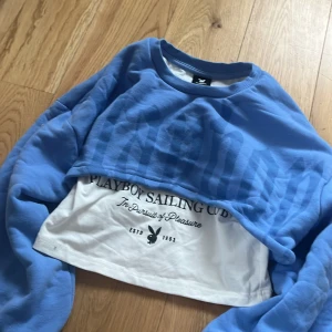 Blå och vit croppad tröja från Playboy - Säljer en cool blå och vit croppad tröja från Playboy med texten 'Playboy Sailing Club' tryckt på framsidan. Tröjan har långa ärmar och en avslappnad passform. Perfekt för en avslappnad stil! Passar en XXS