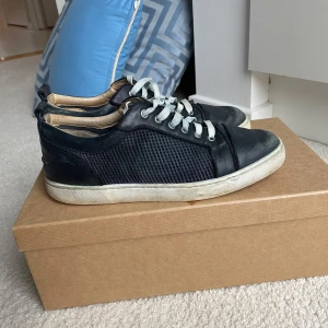 Blå Christian Louboutin skor - Snygga svarta sneakers från Christian Louboutin med den ikoniska röda sulan. Skorna har snörning och en stilren design med meshdetaljer på sidorna. Perfekta för dig som vill ha en touch av lyx i vardagen. Skorna är i skick 5/10 därav priset men inga fler defekter den smuts och skrapmärken