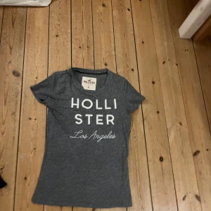 Grå t-shirt från Hollister - Säljer en grå t-shirt från Hollister med texten 'Los Angeles' tryckt på framsidan. T-shirten har en normal passform och korta ärmar, perfekt för en avslappnad stil.