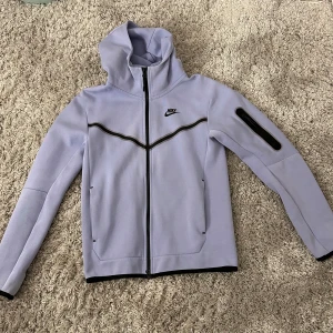 Ljuslila Nike tech flecce XS - Säljer en snygg ljuslila hoddie från Nike med dragkedja och huva. Hoddien har en cool svart detalj på ärmen och en diskret Nike-logga på bröstet. Nypris:1399  Ett litet slit märke på ärmen men inget man tänker på(Säljer syrrans kläder)