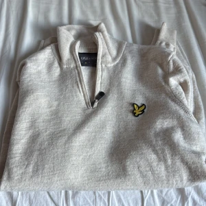 Beige tröja med dragkedja från Lyle & Scott - Säljer en stilren beige tröja från Lyle & Scott med dragkedja och deras ikoniska logga på bröstet. Perfekt för en avslappnad stil. Tröjan har långa ärmar och en bekväm passform. Inga defekter!