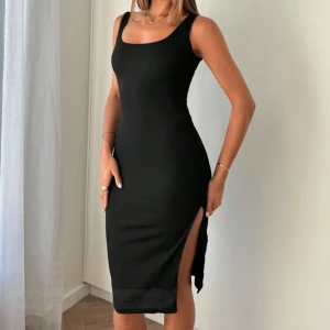 Svart ribbad klänning - Säljer denna snygga svarta ribbade klänningen med  en tight passform och slits på sidan. Perfekt för en stilren look. Klänningen är ärmlös och har en klassisk rund halsringning.