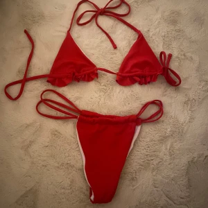 Röd bikini med volangdetaljer - Trendig röd bikini med volangdetaljer och knytband. Toppen har trekantsform och underdelen har knyt i sidorna för justerbar passform. Perfekt för sommarens stranddagar!