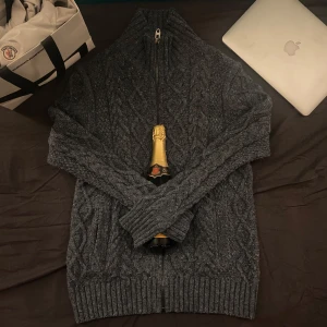 Mörkgrå stickad kofta från Mark Spencer - Säljer en snygg mörkgrå stickad tröja från Mark Spencer North Coast med dragkedja framtill. Tröjan har ett klassiskt flätmönster och hög krage, perfekt för kyliga dagar. Passar både till jeans och chinos. Hör av dig vid intresse!