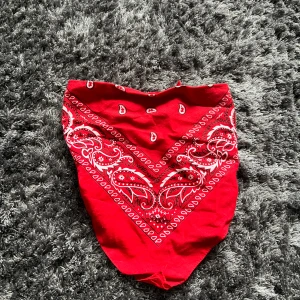 Röd bandana med paisleymönster - Snygg röd bandana med klassiskt paisleymönster. Perfekt som accessoar för att ge en färgklick till din outfit. Kan bäras på flera olika sätt för en personlig stil.