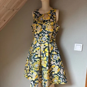 Blommig ärmlös klänning - Säljer en färgglad ärmlös klänning med ett blommigt mönster i gult, svart och vitt. Klänningen har en rund hals och en dragkedja i ryggen. Perfekt för en somrig look!