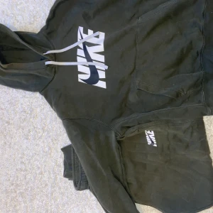 Grön mjukisbyxor och  hoodie från Nike - Säljer en grön hoodie från Nike med stor vit logga på framsidan. Perfekt för en avslappnad stil. Hoodien har en klassisk passform med känguruficka och justerbar huva.
