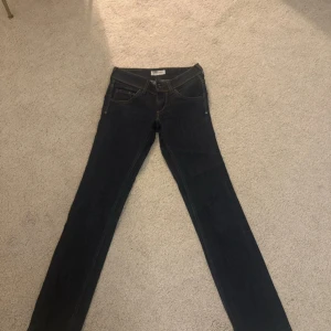 Mörkblå jeans från Lee - Snygga mörkblå jeans från Lee med klassisk femficksdesign och kontrastsömmar. De har en rak passform och stängs med dragkedja och knapp. Perfekta för en stilren look.