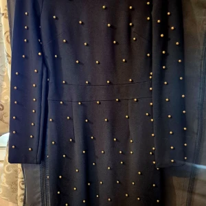 Svart klänning med guld pärlor  - Elegant svart klänning dekorerad med små pärlor över hela ytan. Klänningen har långa ärmar och en figurnära passform som ger en stilren look. Perfekt för en kväll ute eller en speciell tillställning. Klänning har använts bara 1 gång 