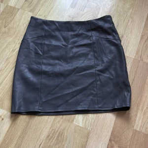 Svart skinnkjol från BikBok - Snygg mörkgrå skinnkjol från BikBok i storlek S. Kjolen har en dragkedja på sidan och en stilren design som passar perfekt för en trendig look. Perfekt för att ge din outfit en edgy touch!