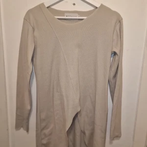 Beige långärmad tröja från XConcept - Säljer en lång tröja från XConcept i stilen avantgarde av tidigare managern för Giorgio Armani, Gabriele Bensi. Den har en unik asymmetrisk design framtill och är tillverkad i ett mjukt material. Perfekt för en futuristisk look. Liten defekt med fläckar, se sista bilden. Därav lågt pris. Kostade runt 150 € i inköp.