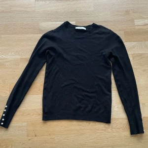 Svart stickad tröja från Zara - Säljer en elegant svart stickad tröja från Zara med långa ärmar och dekorativa pärlor vid ärmsluten. Perfekt för en stilren look. Tröjan är i storlek S och har en klassisk rund halsringning. 💞