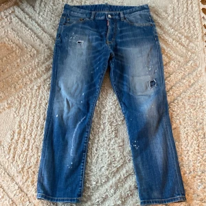  Dsquared2 jeans 14Y - Snygga blå jeansbyxor från Dsquared2 med slitna detaljer och färgstänk för en cool. Modellen på jeansen heter Dsquarde2 Kids teen jeans. Storleken säger 14Y (Står på jeansen). Hör av dig vid frågor!