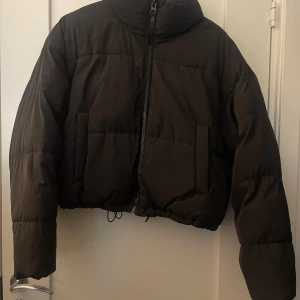 Svart pufferjacka från H&M - Säljer en svart pufferjacka från H&M med dragkedja framtill. Jackan har en hög krage och långa ärmar, perfekt för kyliga dagar. 
