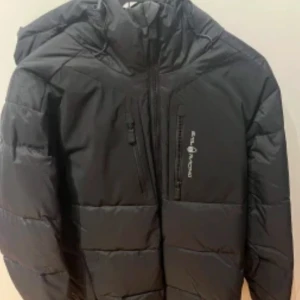 Svart puffer jacket från sail racing - Säljer en stilren svart dunjacka från sail racing. Jackan har en praktisk dragkedja och en justerbar huva. Perfekt för kyliga dagar med sin varma och bekväma design.