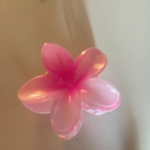 Rosa hårklämma i form av en blomma - Söt rosa hårklämma formad som en blomma. Perfekt för att ge en färgglad touch till din frisyr. Klämman har en glansig yta och är lätt att använda.