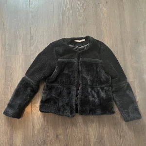 Svart pälsjacka - Säljer en snygg svart pälsjacka med långärmad design. Jackan har en mjuk och fluffig yta med stilrena detaljer. 