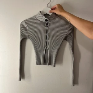 Grå ribbad tröja - Säljer en stilren grå ribbad kofta med långa ärmar och hål framtill. Perfekt för lager-på-lager och ger en snygg look till vardagsoutfiten. Passar bra till både jeans och kjol.