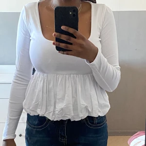 Vit långärmad topp från Zara - Säljer en vit långärmad topp från Zara med en v-ringad design och volangdetaljer i nederkant. Perfekt för en stilren look.