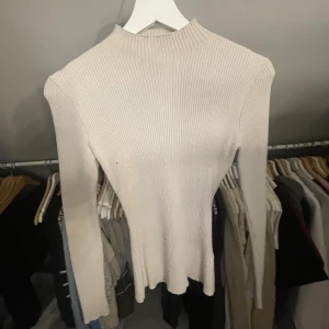 Beige ribbad tröja från H&M - Säljer en stilren beige ribbad tröja från H&M. Tröjan har en hög hals och långa ärmar. 