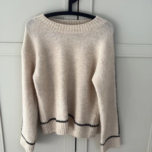 Beige stickad tröja från Lindex - Säljer en mysig beige stickad tröja från Lindex med svarta detaljer. Tröjan har långa ärmar och ribbstickade muddar vid ärmslut. Den är helt oanvänd🩷