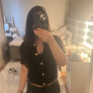 Svart kofta med guldknappar - Snygg svart kofta med korta ärmar och dekorativa guldknappar framtill. Perfekt för att lägga till en touch av elegans till din outfit. Pris kan diskuteras💞