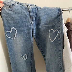 Blå jeans med hjärtdetaljer - Snygga blå jeans med unika hjärtdetaljer på framsidan. Perfekta för att ge din outfit en personlig touch. Klassisk femficksdesign och bekväm passform.