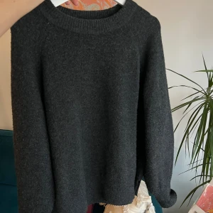 Mörkgrå stickad tröja - Säljer en mysig mörkgrå stickad tröja med rund halsringning. Perfekt för kyliga dagar och enkel att matcha med olika outfits. Tröjan har långa ärmar och en avslappnad passform och diskret snittad ned till 