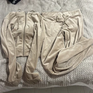 Beige mjukisbyxor med dragkedja det  - Säljer ett par beige mjukisbyxor med matchande huvtröja. Byxorna har en bekväm passform med knytning i midjan och vida ben. Huvtröjan har dragkedja och fickor framtill, perfekt för en avslappnad stil. Lite använd. Storlek M på båda. 95% polyester, 5% elastan. Skriv för eventuella frågor 🌸 kolla gärna in mina andra annonser!⤵️✨