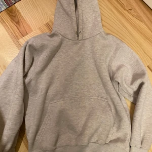 Grå hoodie - Gråmelerad hoodie med luva och ficka fram. Muddar i ärmslut och nederkant.  Strl S. 