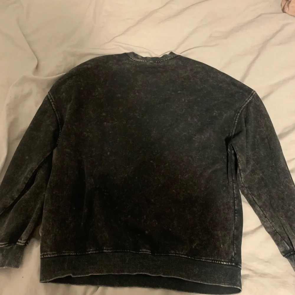 Cool svart oversized sweatshirt med tryck av The Cure på framsidan. Tröjan har en vintage-look med ett stort tryck i lila och vit text. Perfekt för fans av bandet eller för en avslappnad stil.. Neuletakit & Villapaidat.