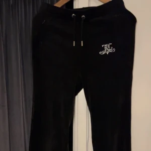 Svarta mjukisbyxor från Juicy Couture - Snygga svarta mjukisbyxor från Juicy Couture med glittrande Juicy-logga på framsidan och baksidan. Juicy loggan är av den äldre typen och säljs inte längre. Byxorna har en bekväm passform med snörning i midjan för justerbarhet. Perfekta för en avslappnad stil.💕