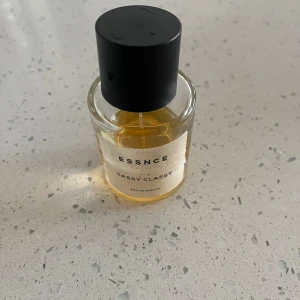 Parfym ESSNCE Sassy Classy - Säljer en elegant parfymflaska från ESSNCE med doften Sassy Classy. Flaskan är genomskinlig med en svart kork och innehåller en gyllene vätska. Perfekt för den som vill ha en sofistikerad och stilren doft. Lite mindre än halva kvar!