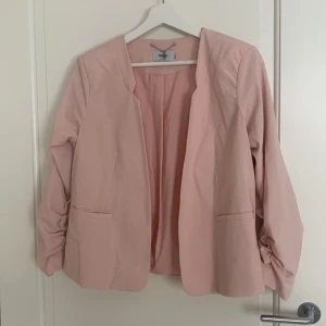 Ljusrosa kavaj från Only - Säljer en stilren ljusrosa kavaj från Only. Den har en öppen design utan knappar och halvlånga ärmar med rynkade detaljer. Perfekt för att ge en elegant touch till din outfit. Lite smått nopprig på vissa ställen. Använd en hel del men fortfarande fint skick! Storlek 38. 