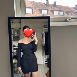 Svart offshoulder klänning - Snygg svart offshoulder klänning med tight passform och rynkade detaljer. Perfekt för en kväll ute eller en speciell tillställning. Klänningen har långa ärmar och en kort längd som ger en elegant look.