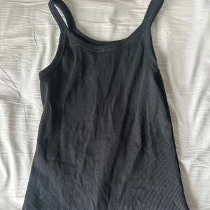 Svart ribbad linnetopp från SOC - Säljer en svart ribbad linnetopp från SOC. Perfekt för en avslappnad stil med smala axelband och en bekväm passform. Passar bra till både jeans och kjol.