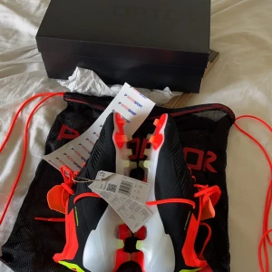 Adidas Predator fotbollsskor - Snygga Adidas Predator fotbollsskor i svart med vita och röda detaljer. Skorna har en modern design med snörning och är perfekta för fotbollsplanen. De har en iögonfallande röd insida och gula detaljer som ger en extra touch. Det är använde 1 gång på konstgräs tod bort prislappen på skon eftersom ja skulle träna med de, nu är du splitternya och bara ligger hemma för att de är försmå. Storleken är 43 1/3 men det är små i storleken jag kunde ha de när ja hade 42 1/2   Alla frågor är välkommen 🤗 