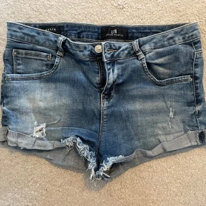  jeansshorts LTB - Snygga blå jeansshorts från LTB med fransiga kanter och slitna detaljer. Perfekta för en avslappnad stil. De har fem fickor och en knappgylf.