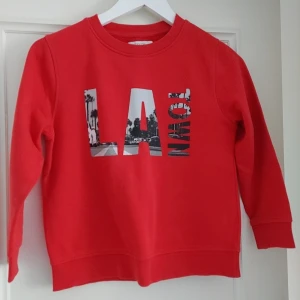Röd tröja från Zara Kids - Säljer en cool röd tröja från Zara Kids med trycket 'LA' i svartvitt. Perfekt för barn som gillar en urban stil. Tröjan har långa ärmar och en rund halsringning.