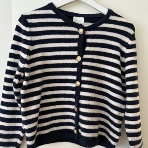 Randig kofta från H&M - Säljer en snygg randig kofta från H&M i mörkblå och vit. Koftan har långa ärmar och knäpps med stiliga knappar framtill. Perfekt för en avslappnad stil.