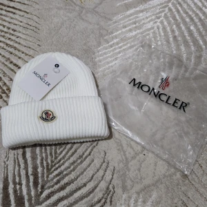 Vit ribbad mössa  - Säljer en stilren vit ribbad mössa från Moncler. Mössan har en broderad logotyp framtill och är perfekt för kyliga dagar. Den kommer med originalförpackning och etikett.