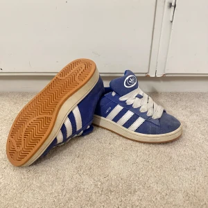 Blå Adidas Campus sneakers - Snygga blå Adidas Campus sneakers med vita ränder och snörning. Några slitningar och lite smutsiga (se bilder). Perfekta nu för vår och sommar! Pris kan diskuteras!
