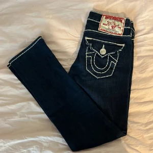 Mörkblå jeans från True Religion - Snygga mörkblå jeans från True Religion med kontrasterande vita sömmar och unika bakfickor med knappar. Dock så finns det en liten del av sömmen som är av och därav lite lägre pris.(fråga om bild) Jeansen har en klassisk femficksdesign och en knappgylf. Perfekta för en stilren look. Använda fåtal gånger av mig och förra ägaren, sammanlagt ca 10 gngr. Skulle säga att de fof är i ganska bra skick! Inte fast pris men runt 800