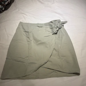 Ljusgrön omlottkjol - Säljer en ljusgrön omlottkjol från H&M Divided med knyt i midjan. Kjolen är kort och har en enkel, stilren design. Tillverkad i  bomull.