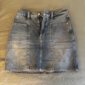 Jeanskjol från Calvin Klein - Säljer en klassisk blå jeanskjol från Calvin Klein med fickor fram och bak samt knapp- och dragkedjestängning. Aldrig använd, och passar xs-s(34)