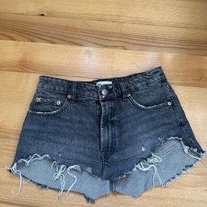 Svarta jeansshorts med fransar från Zara 38 - Säljer ett par svarta jeansshorts från Zara med råa franskantade benslut och klassisk femficksmodell. Shortsen har låg midja och slitna detaljer för en cool look. Perfekta för sommaren! Dragkedja som gylf.