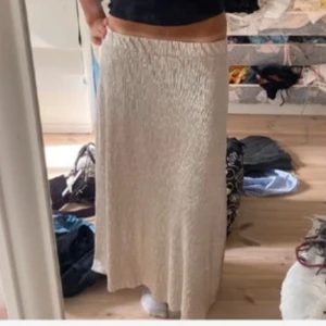 Beige långkjol i plisserat material - Säljer en beige långkjol med plisserad struktur och elastisk midja. Kjolen har en flowy passform och är perfekt för dig som gillar en stilren och enkel look. Passar till många olika outfits och är superbekväm.❤️